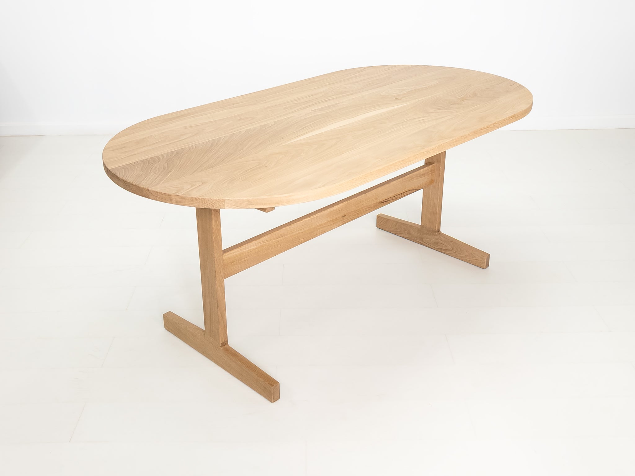 Custom wood dining table with clean lines and trestle base, shown in natural white oak.