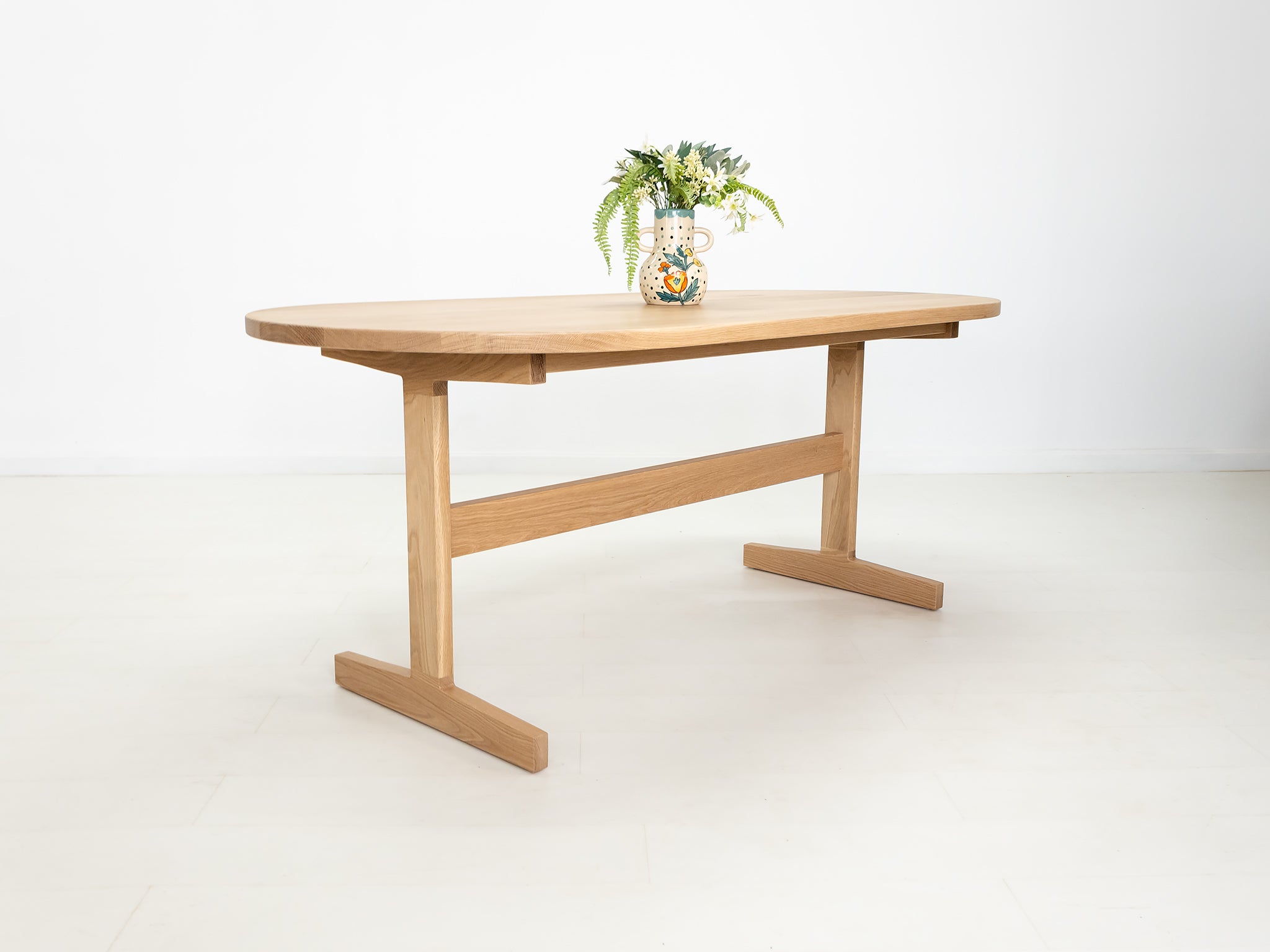Custom wood dining table with clean lines and trestle base, shown in natural white oak.