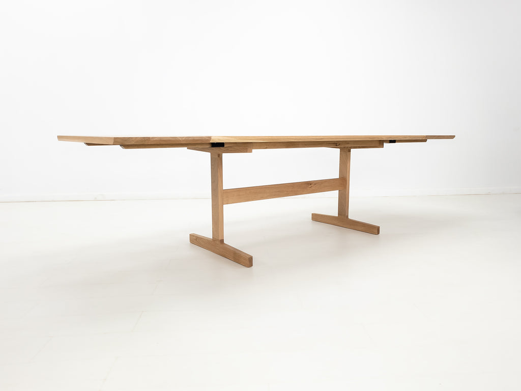 BRIT trestle dining table in natural white oak, shown with beveled edge top and coordinating extensions.