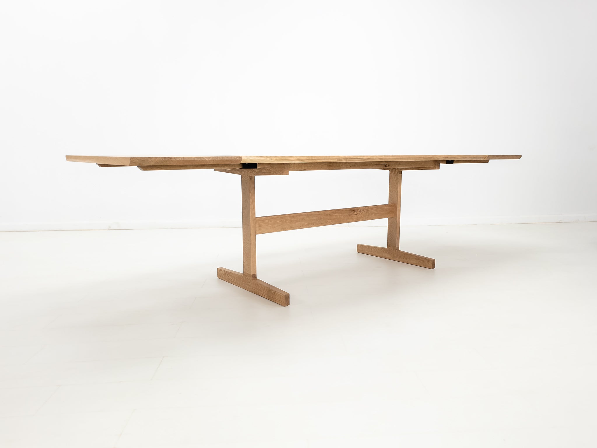 BRIT trestle dining table in natural white oak, shown with beveled edge top and coordinating extensions.