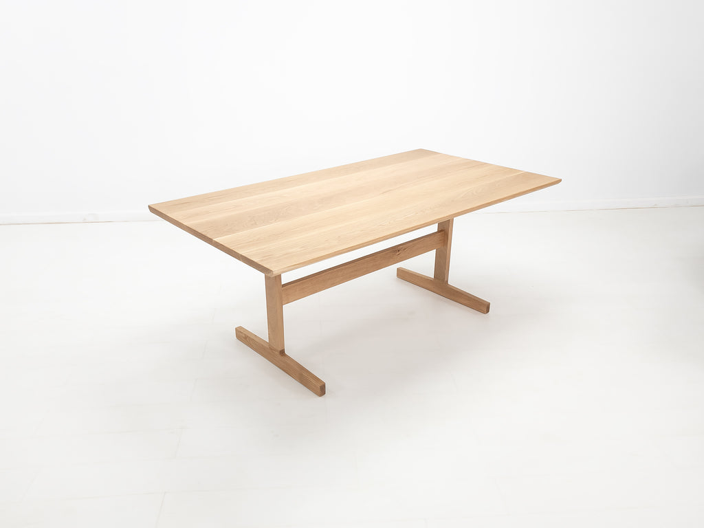 BRIT trestle dining table in natural white oak, shown with beveled edge top and clear matte finish.