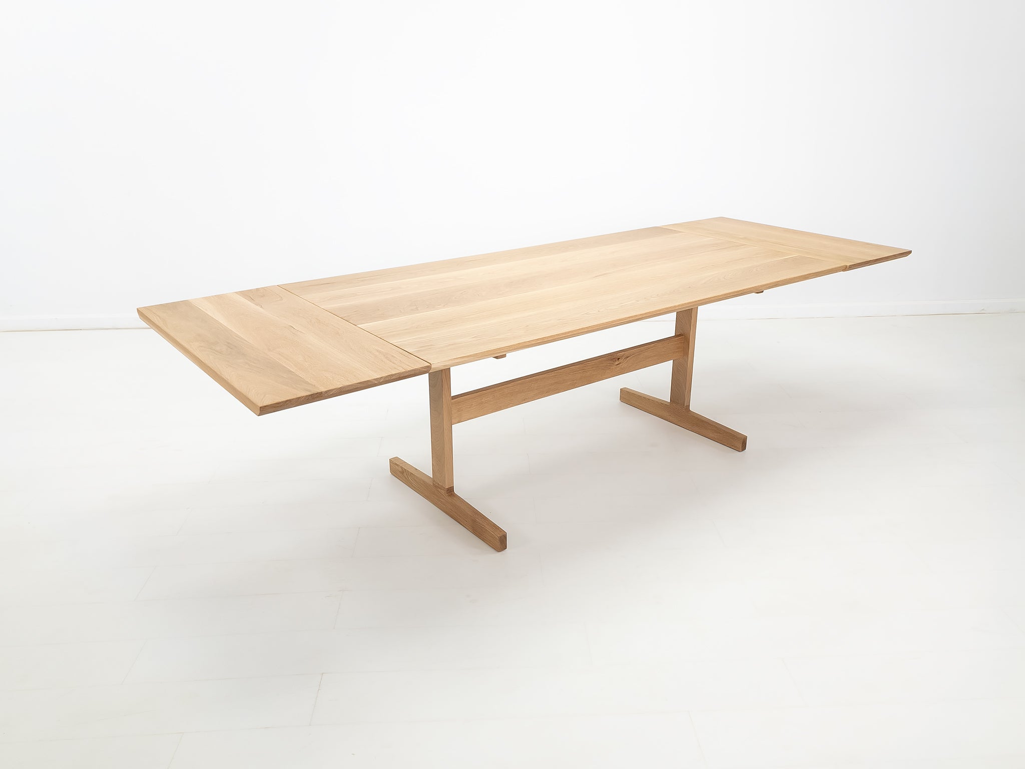 BRIT trestle dining table in natural white oak, shown with beveled edge top and coordinating extensions.