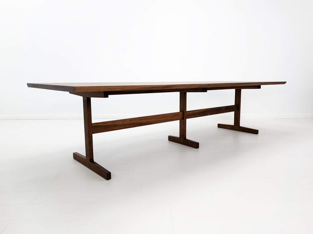 BRIT trestle dining table in oiled walnut, shown with beveled edge top and hardwax oil finish.