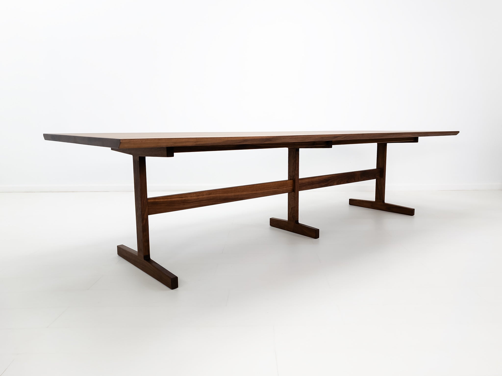 BRIT trestle dining table in oiled walnut, shown with beveled edge top and hardwax oil finish.