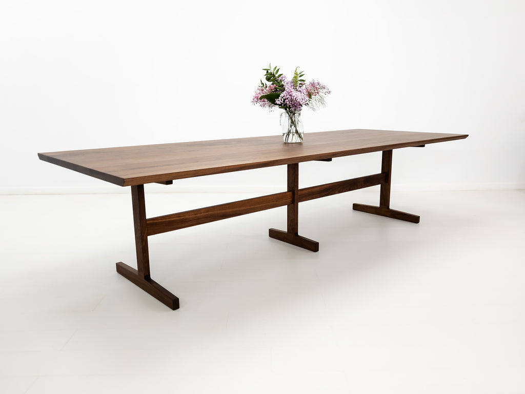 BRIT trestle dining table in oiled walnut, shown with beveled edge top and hardwax oil finish.