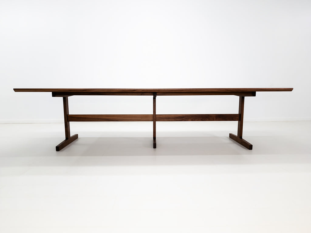 BRIT trestle dining table in oiled walnut, shown with beveled edge top and hardwax oil finish.