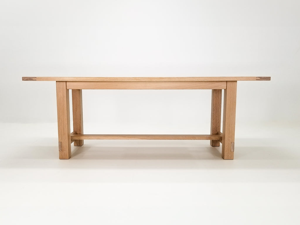 Studio shot of Rémy table showing exposed joinery and full trestle-style base.