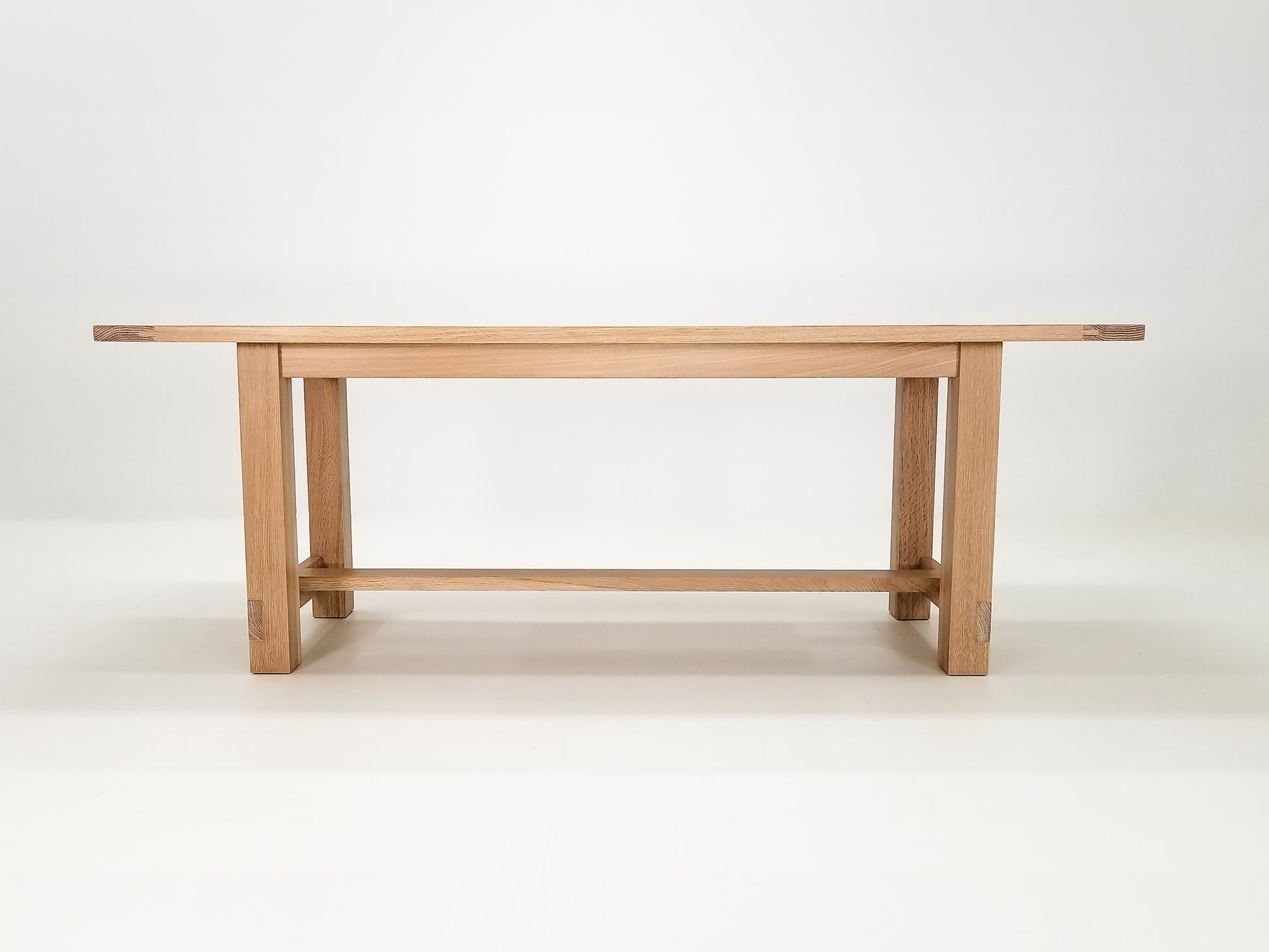 Studio shot of Rémy table showing exposed joinery and full trestle-style base.
