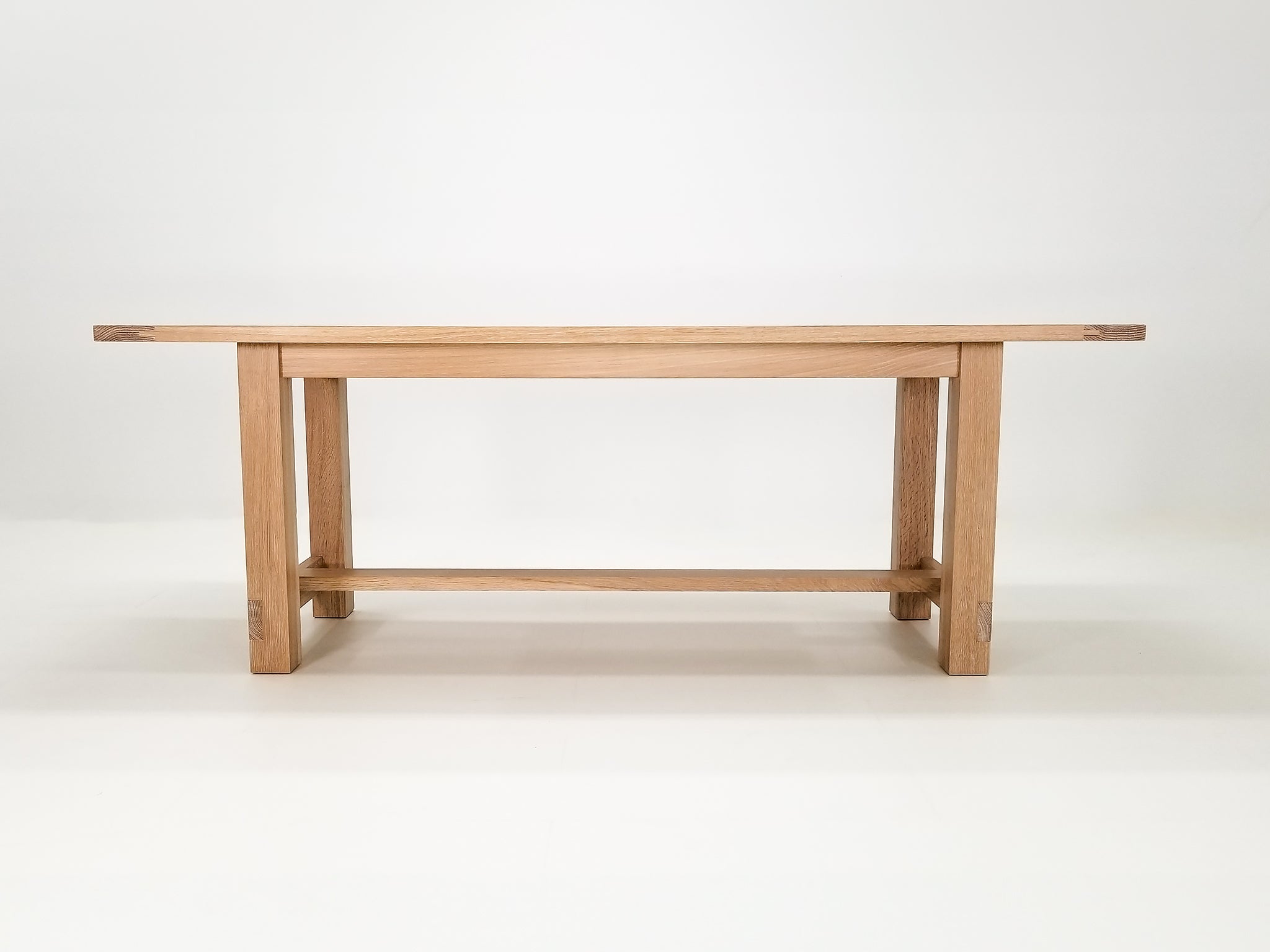 Studio shot of Rémy table showing exposed joinery and full trestle-style base.