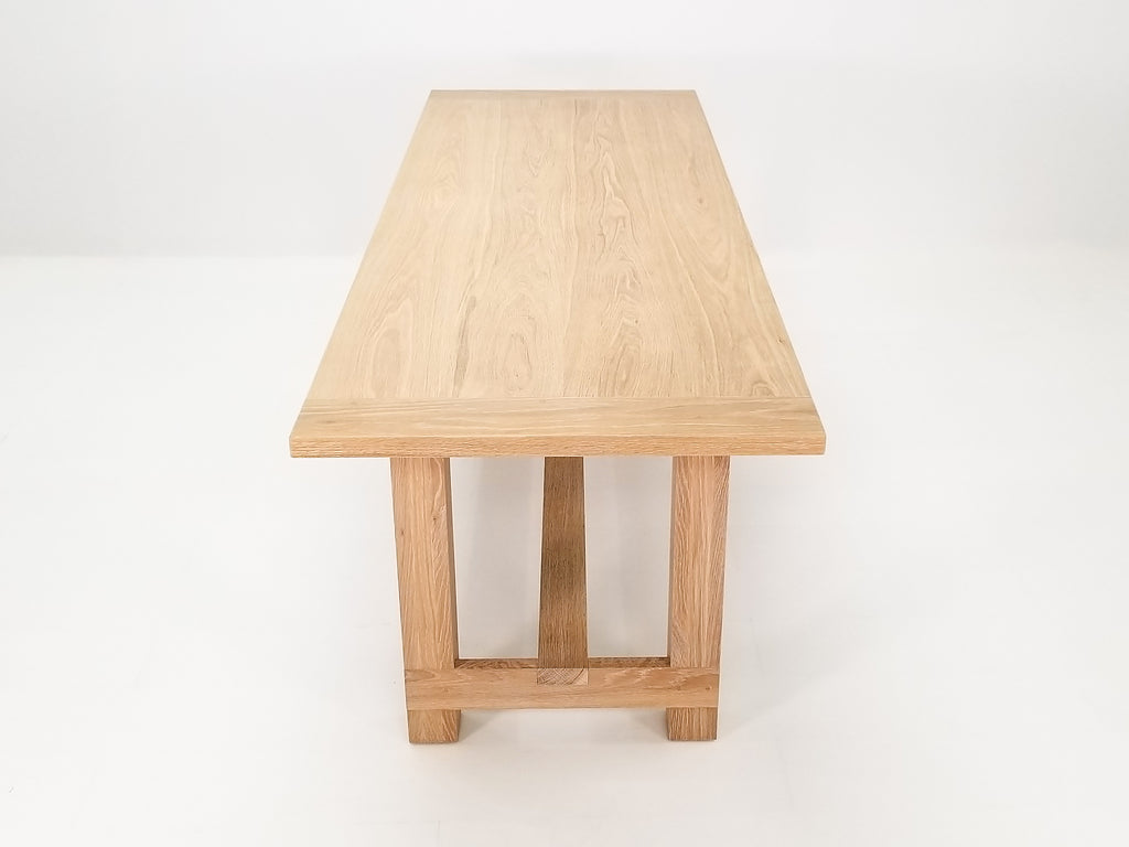 Studio shot of Rémy table showing exposed joinery and full trestle-style base.