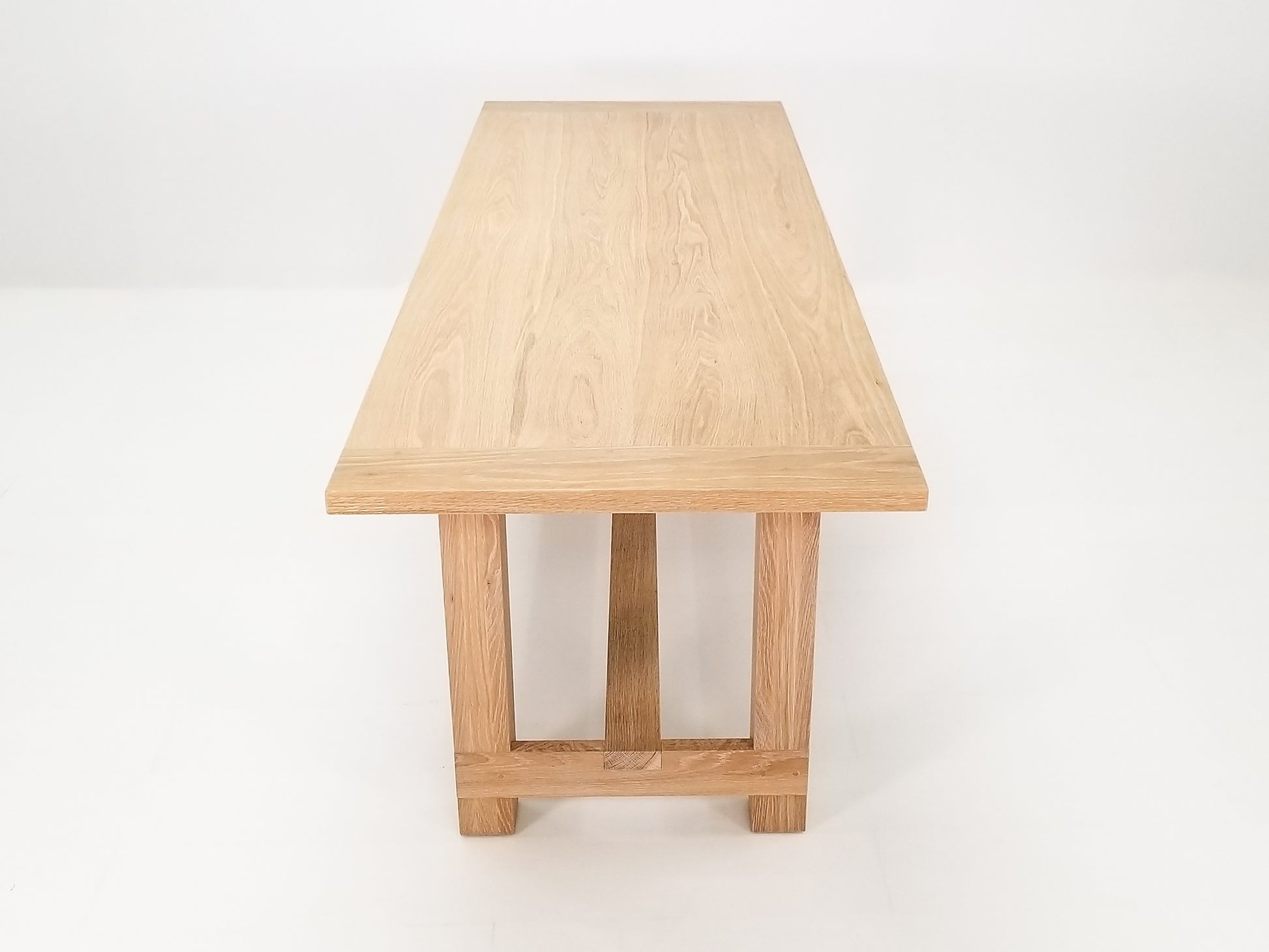 Studio shot of Rémy table showing exposed joinery and full trestle-style base.