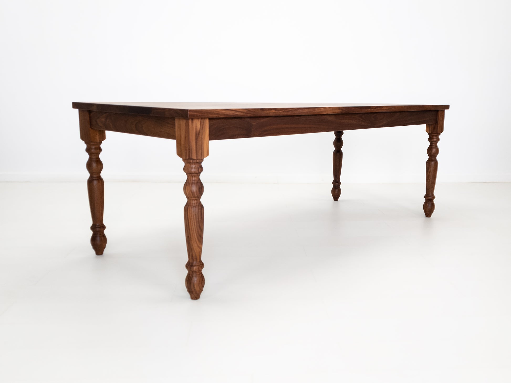 Tess dining table in solid oiled walnut with turned legs and plank-style top.