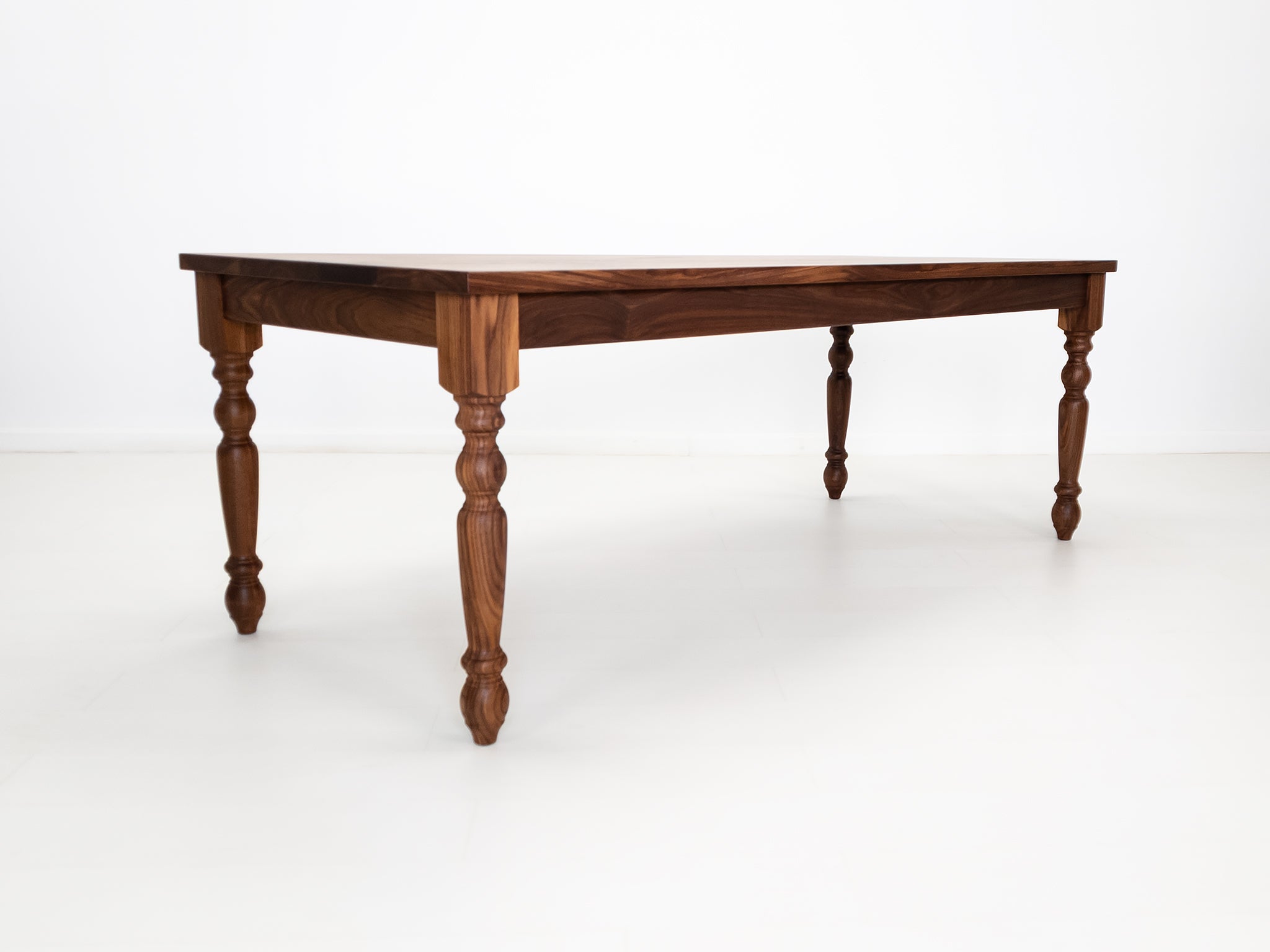 Tess dining table in solid oiled walnut with turned legs and plank-style top.