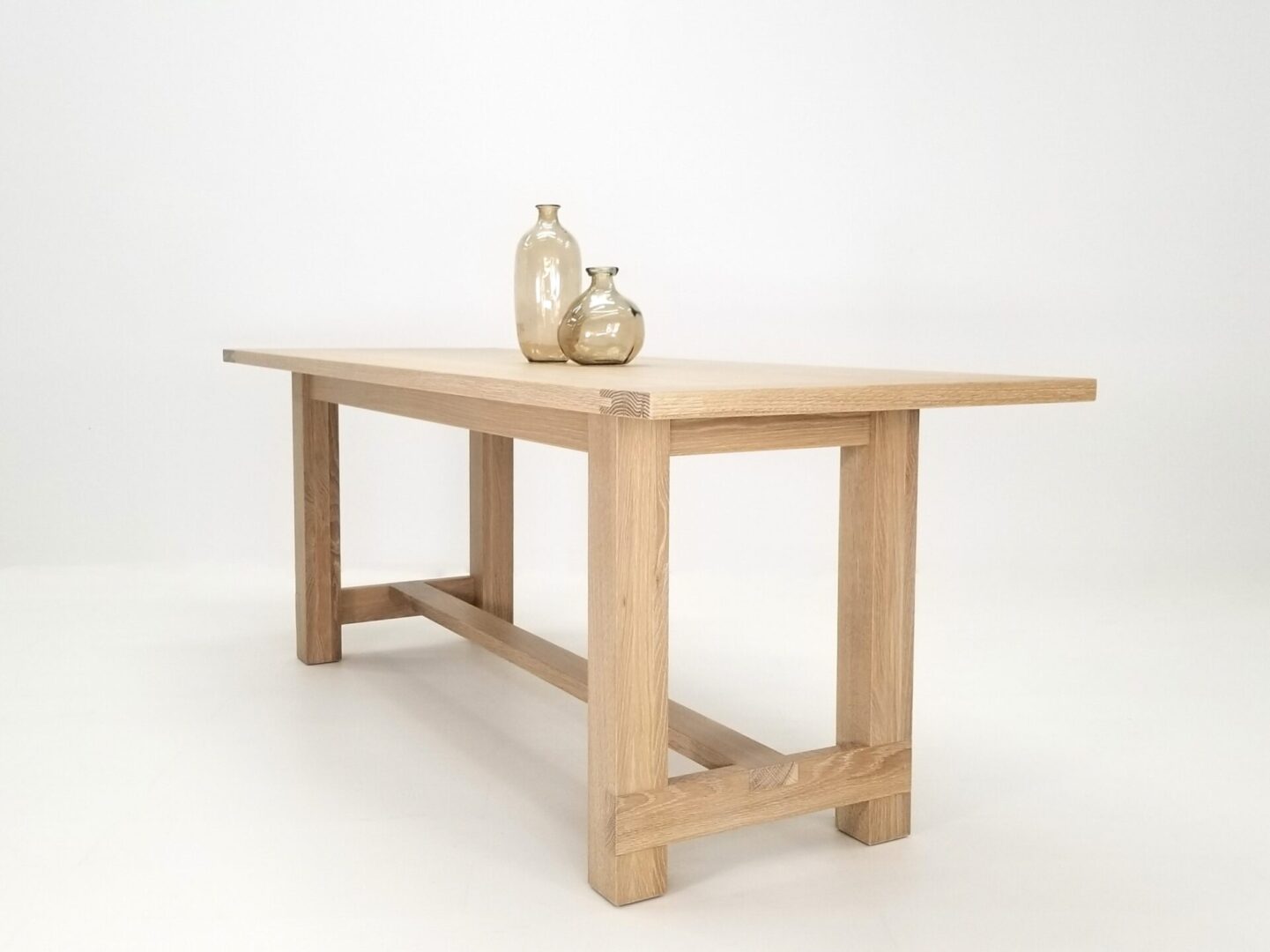 A white oak trestle table with vases on top of it.