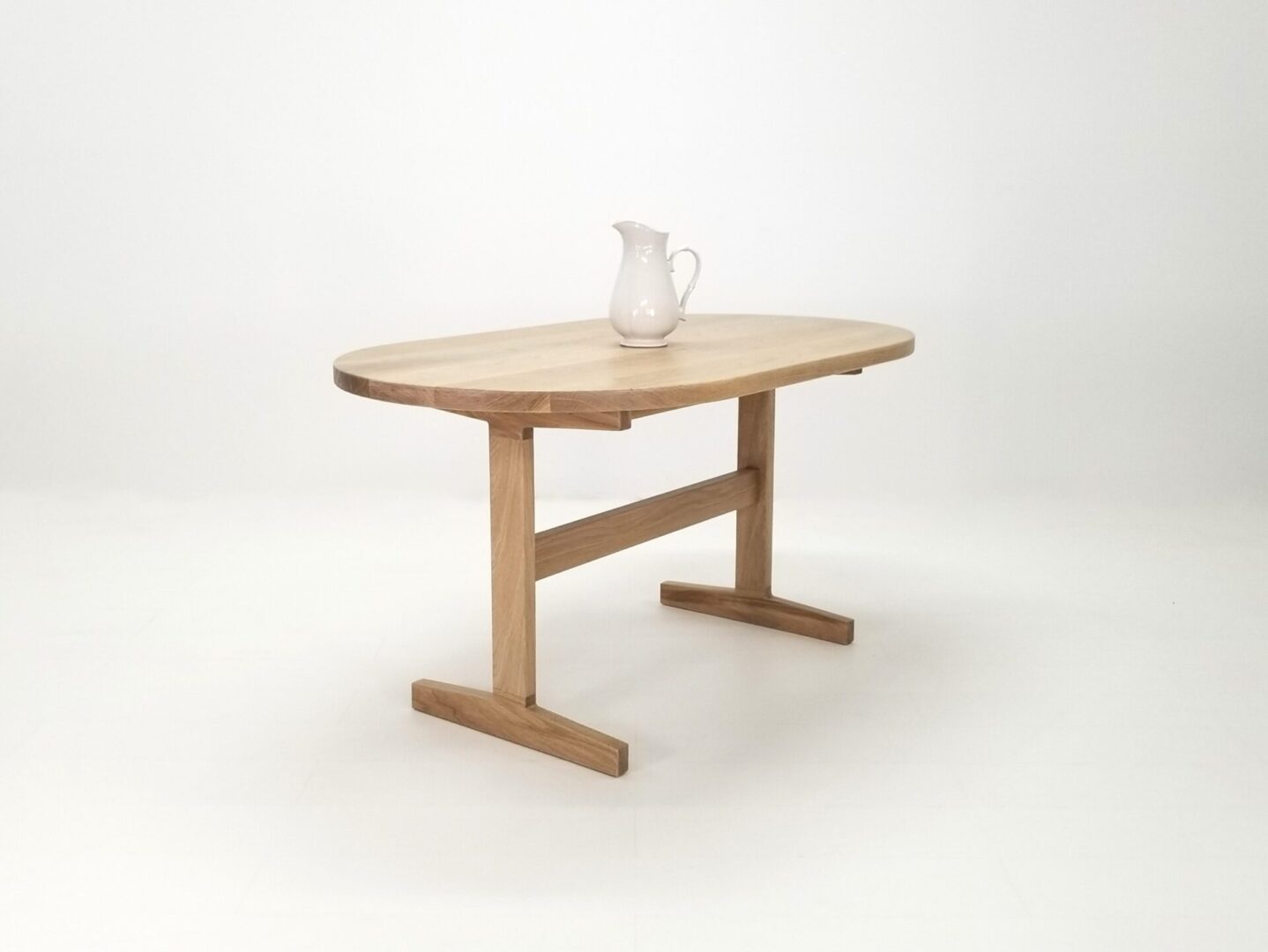 A oval top trestle dining table with a pitcher on top.