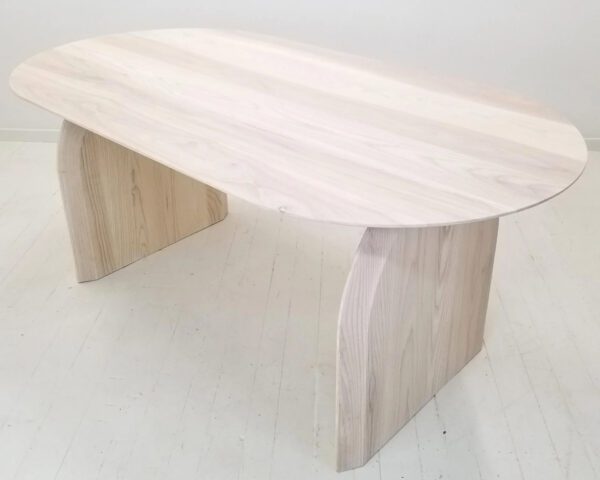 A sunwashed ash dining table with a curved top and legs.