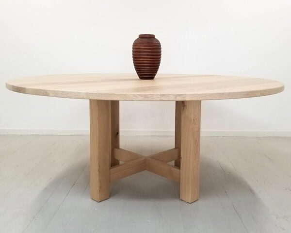 A round dining table with a trestle base and a vase on top.