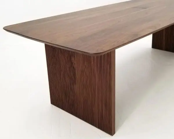 A close up of a walnut wooden table with ribbed legs.