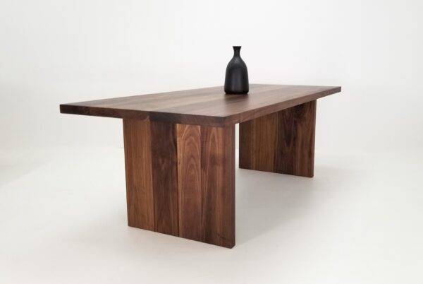 A 2" thick walnut dining table with a vase on top of it.