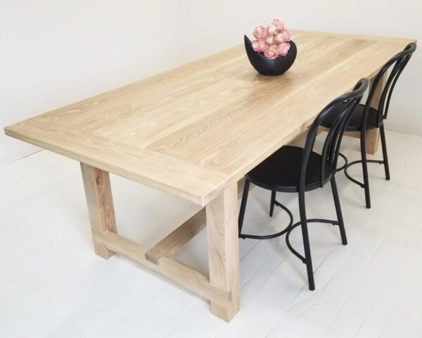 A seawashed white oak trestle dining table with a vase on top.