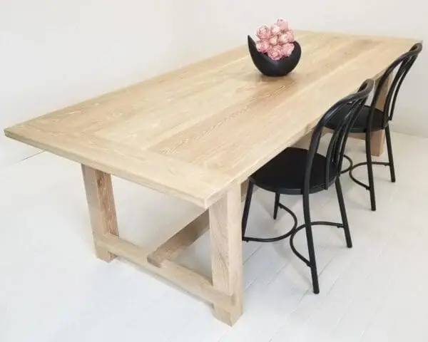 A seawashed white oak trestle dining table with a vase on top.