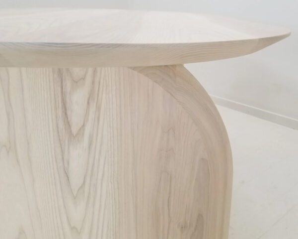 A sunwashed ash dining table with a curved top and legs.