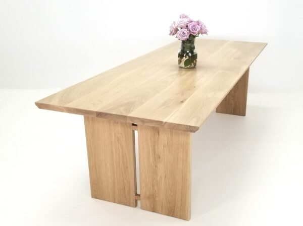 A DIVI dining table with split panel legs and flowers in a vase.