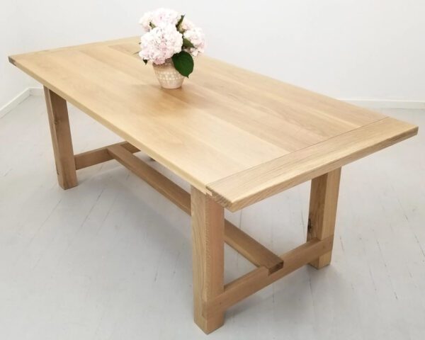 A natural white oak trestle dining table with a vase on top.