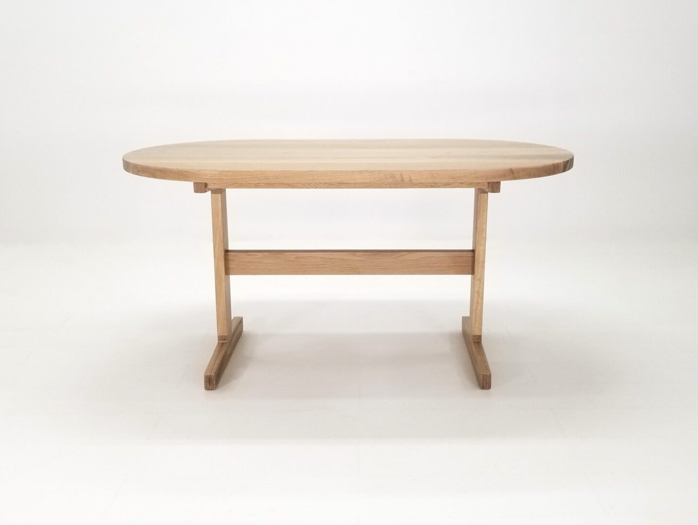 A oval top trestle dining table with a round top and two legs.
