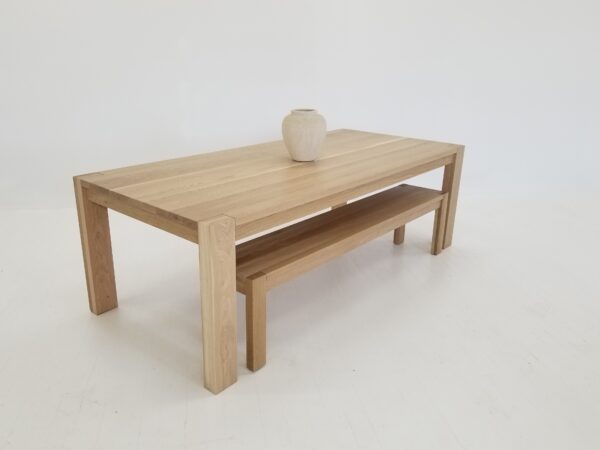 A white oak dining table with a vase on top and a solid white oak bench next to it.