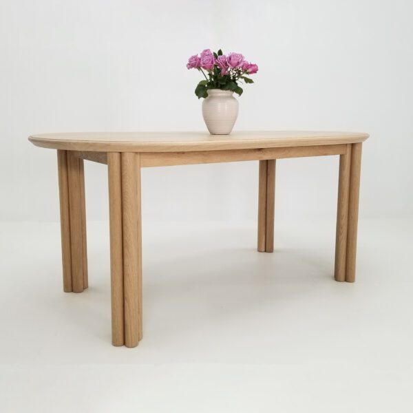 A cylinder leg dining table with four legs and a vase on top.