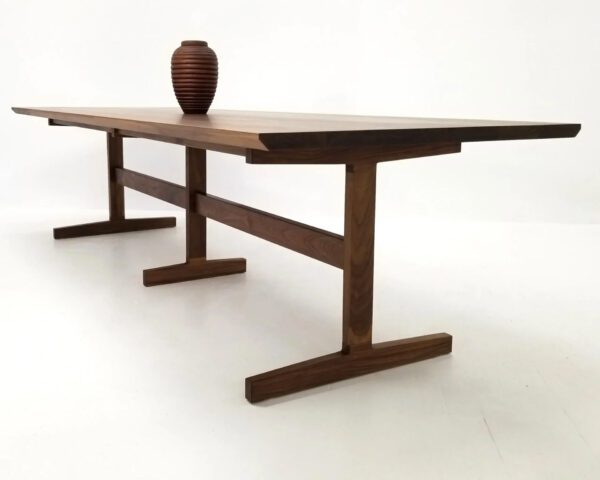 A walnut dining table with three legs and a vase on top.