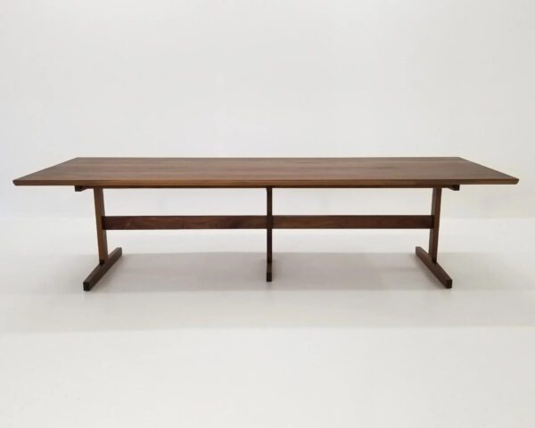 A walnut dining table with three legs and a beveled edge.