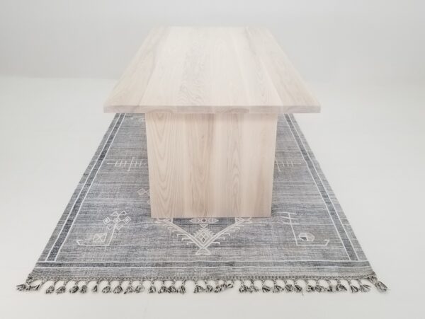 A LILY 1.5 panel dining table with a tassel rug on top.