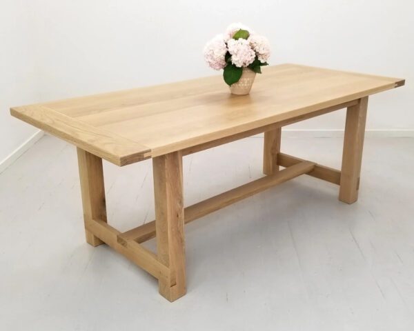 A natural white oak trestle dining table with a vase on top of it.