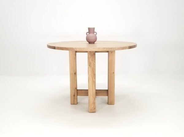 A round white oak dining table with a vase on top of it.