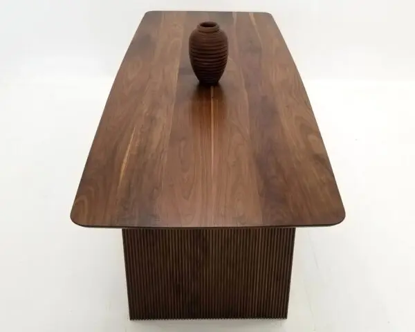 A walnut wooden table with ribbed legs and a vase on top.