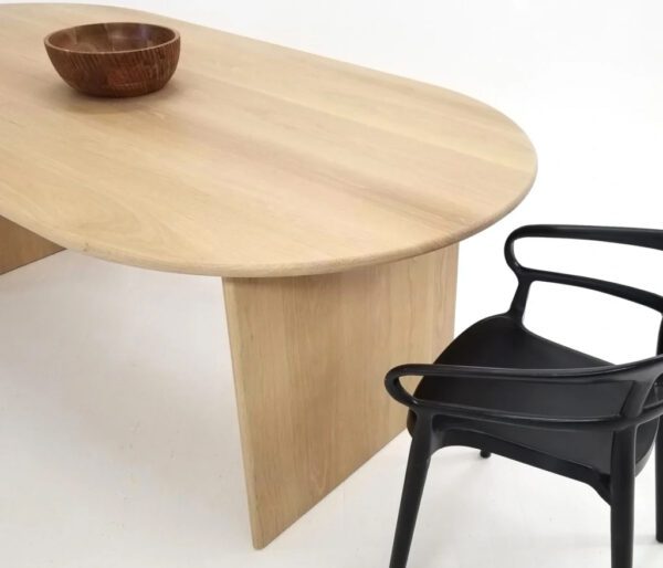 A wooden dining table with a curved top and a chair next to it.