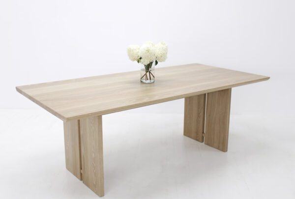 A wooden dining table with split panel legs and flowers on top.