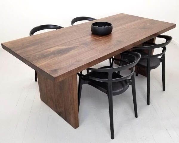 A 2 inch thick solid walnut dining table with a bowl on top of it and chairs around it.
