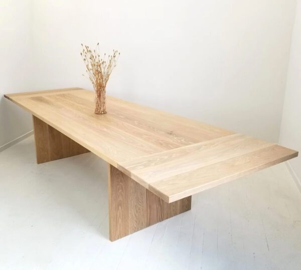 White oak panel dining table with vase on top.
