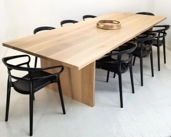 White oak panel dining table with sleek black chairs around it.