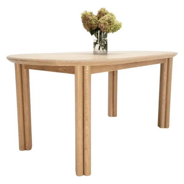 A close up of a white oak dining table with cylinder legs and a vase full of flowers on top.