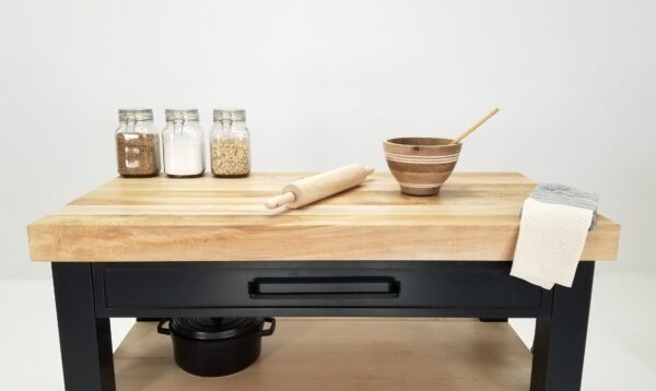 A close up of a black butcher block kitchen island with shelves underneath it.