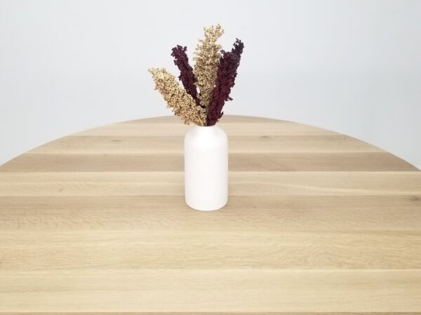 A natural white oak round dining table with a vase on top of it.