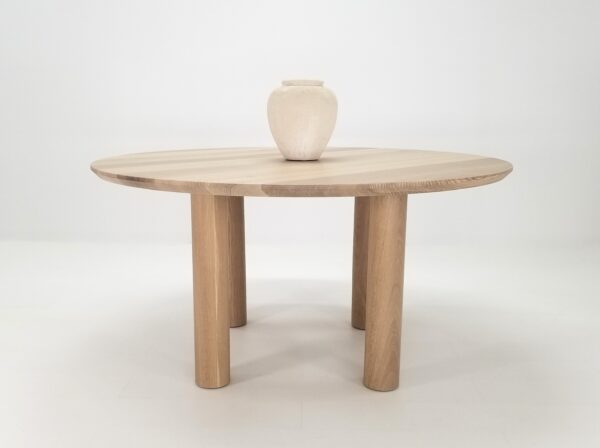 A natural white oak round dining table with a vase on top of it.