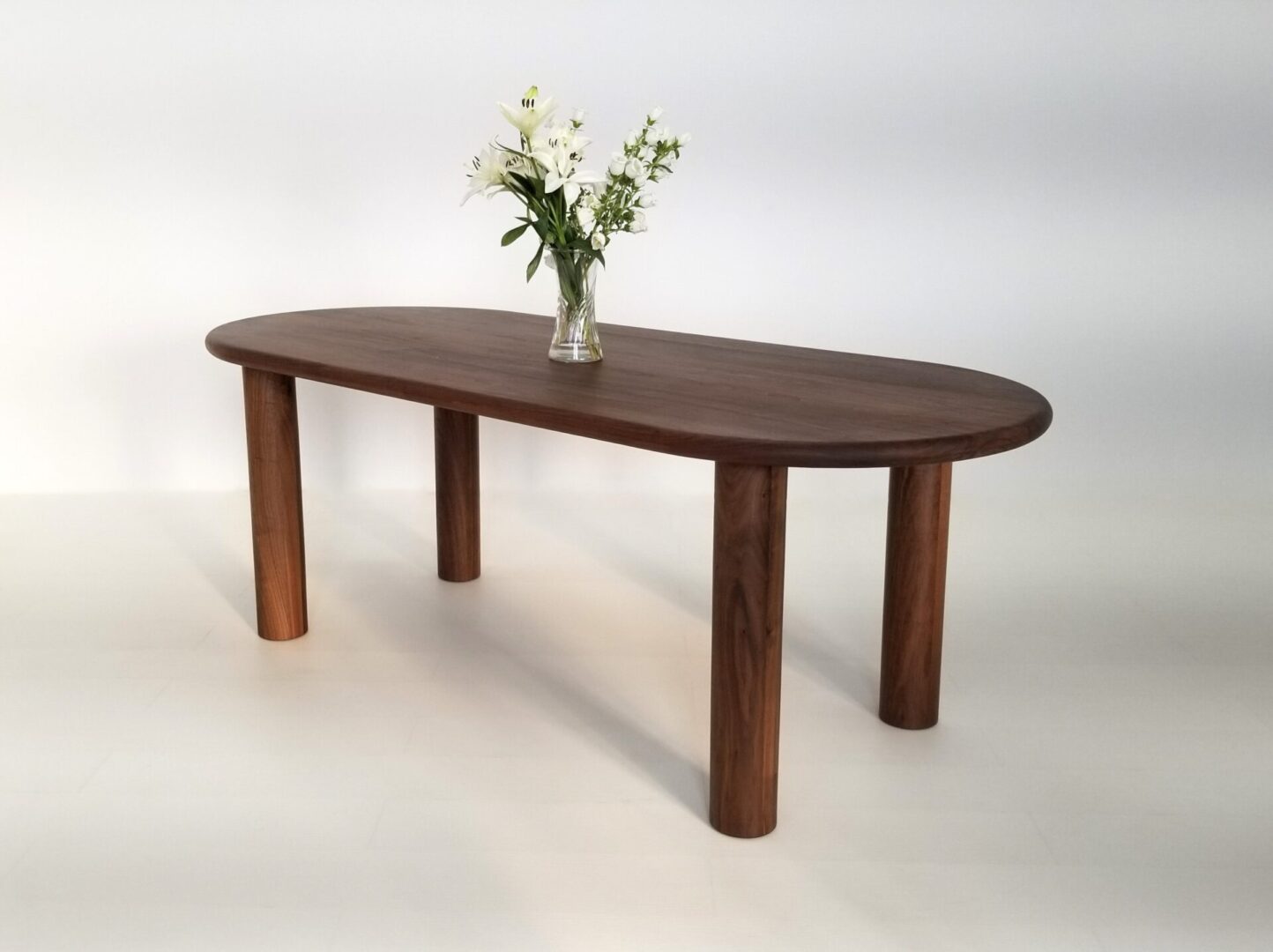 A oval walnut dining table with a vase and flowers on top.