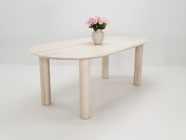 Our oval top COVE dining table in sunwashed ash, with a vase on top of it.