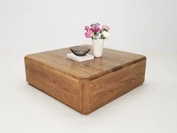 A square coffee table with a vase on top of it.