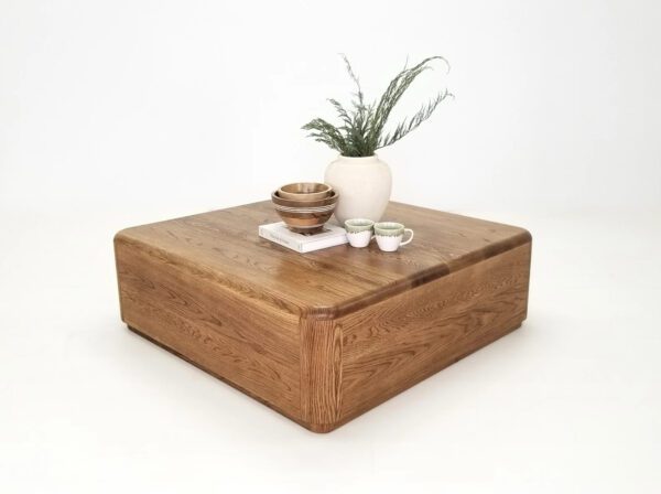 A square coffee table with a vase on top of it.